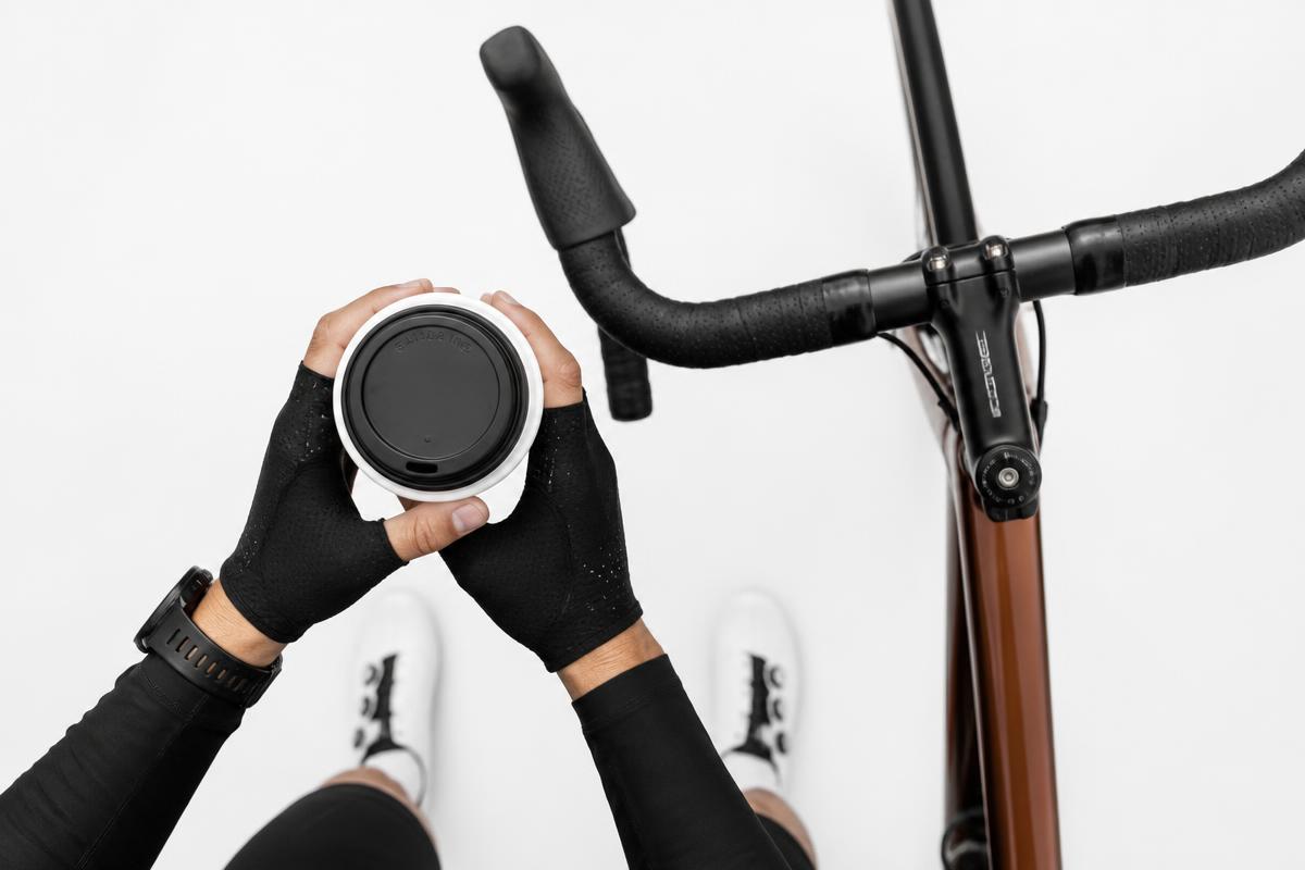 Cyclist holding a takeaway coffee cup next to a road bike